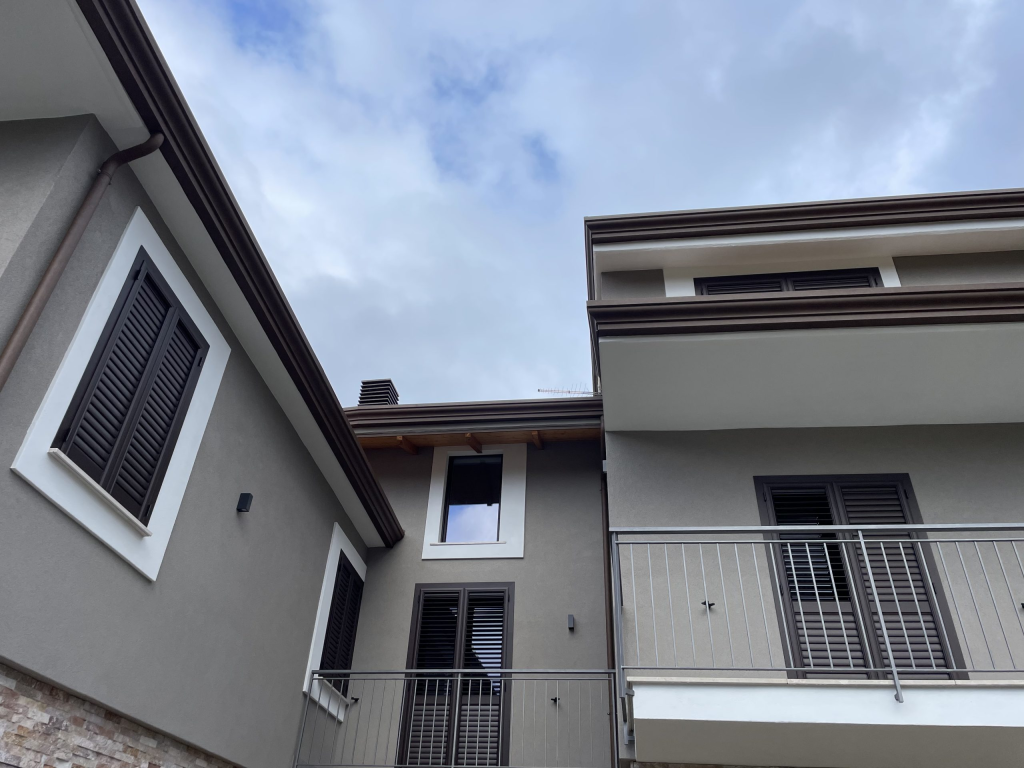 Dettagli Architettonici. Finiture moderne e pulite: facciata intonacata color tortora e infissi in contrasto scuro. Un design essenziale che valorizza l'efficienza energetica